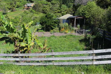 A imagem retrata uma paisagem rural serena com um campo verde exuberante com árvores, um riacho sinuoso e uma pequena vila ao fundo, evocando uma sensação de tranquilidade e beleza natural.