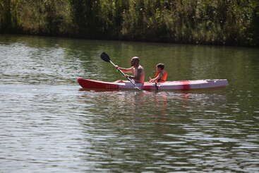 Un hombre y un niño reman en un kayak rojo y blanco en un río tranquilo, rodeados de árboles verdes, disfrutando juntos de una tranquila aventura al aire libre.