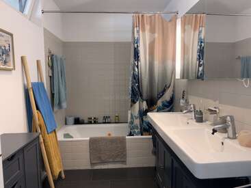 Este moderno cuarto de baño cuenta con un lavabo doble, una bañera con una cortina de ducha con motivos ondulados, toalleros con toallas de colores, un gran espejo y artículos de aseo organizados.