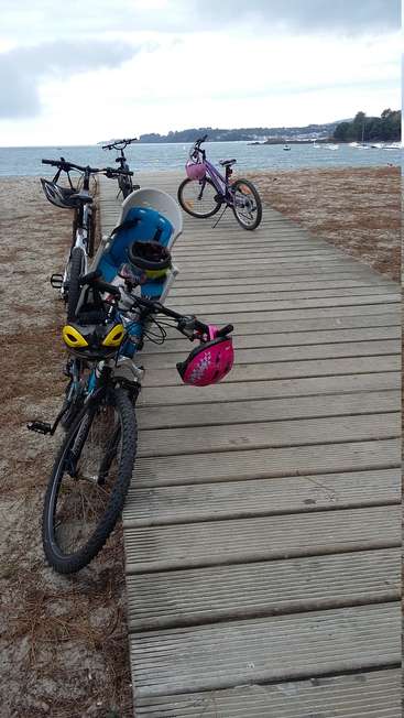 Das Bild zeigt eine ruhige Strandszene mit Fahrrädern, die auf einer hölzernen Strandpromenade geparkt sind, mit Blick auf das Meer und den bewölkten Himmel.