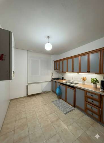 A clean, modern kitchen with tiled floors, blue and wood cabinets, a double sink, countertop appliances, under-cabinet lighting, a window, radiator, and pendant ceiling light.