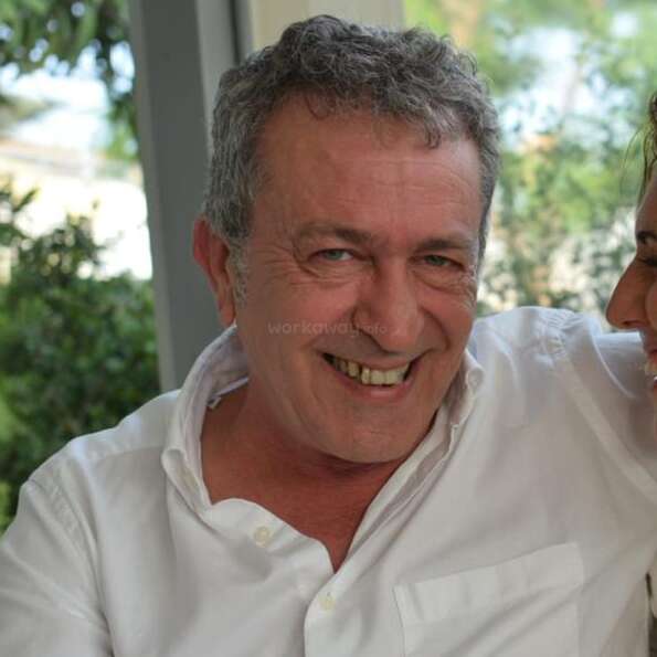 The image shows a man and woman embracing, with the man\'s arm around the woman\'s shoulder, set against a natural outdoor background. The scene is likely a romantic one.