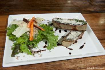 Das Bild zeigt einen weißen Teller mit einem Salat und zwei Fleischscheiben vor einem Holztisch-Hintergrund. Der Salat besteht aus gemischtem Grün, geraspeltem Käse und einer Karotte als Beilage.
