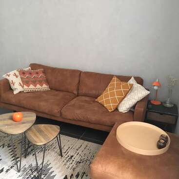 The image depicts a cozy living room with a brown couch, wooden tables, and a rug, featuring a harmonious blend of earthy tones and decorative elements.