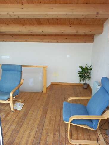 Esse loft aconchegante tem piso e teto de madeira, duas poltronas azuis almofadadas, um vaso de plantas, um pequeno aquecedor e uma revista colocada no chão.