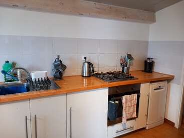 Esta imagem mostra uma bancada de cozinha com pia, escorredor de pratos, utensílios, chaleira elétrica, fogão, forno, máquina de lavar louça, cafeteira e vários itens de cozinha.