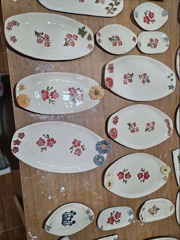Several oval plates and small dishes with floral designs are arranged on a wooden table. The ceramics have hand-painted red, blue, and yellow flowers.