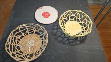 Three handcrafted ceramic bowls sit on a dark table: two are openwork designs with intricate patterns, and one is a plate with a red rose motif.
