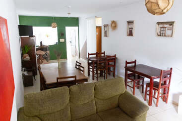This image shows a cozy dining and living area with a green couch, rustic wooden tables and chairs, green accent wall, wall decor, and plenty of natural light.