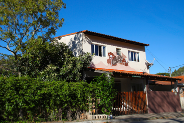 This image shows a two-story building with a red-tiled roof, surrounded by green foliage. The building features a sign with a dog illustration and the words “Ado Milan Pet.”