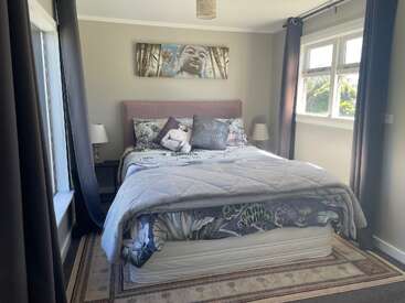 Una acogedora habitación con una cama de matrimonio con ropa de cama estampada, suaves tonos grises, lámparas de noche, cortinas oscuras, grandes ventanas y un sereno cuadro de Buda en la pared.