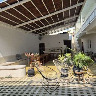 The image depicts a spacious room with a high ceiling, featuring a staircase, plants, and chairs, with a man walking down the stairs in the background.