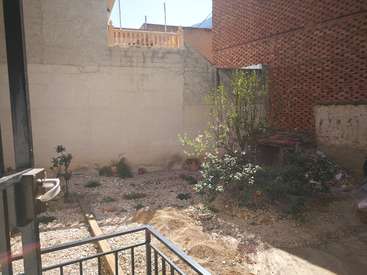 La imagen muestra un pequeño patio exterior con superficie de grava, algunas plantas y una barandilla, rodeado por un muro de hormigón y un edificio de ladrillo.