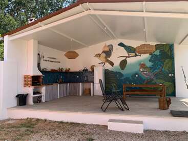Cette photo montre une cuisine en plein air avec une fresque représentant des oiseaux sur le mur du fond, un coin repas, un barbecue, un évier, du carrelage bleu et des meubles en bois naturel.