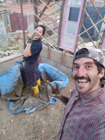 Un homme et une femme souriants travaillent ensemble sur un projet de construction, mélangeant de la boue avec leurs mains et leurs bottes, profitant de l'activité en plein air et prenant un selfie joyeux.