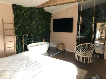 Cette chambre élégante dispose d'une baignoire indépendante, d'un mur de plantes vertes, d'une télévision à écran plat, d'une chaise suspendue, d'une échelle en bois et d'une décoration confortable inspirée de la nature avec des tons terreux.