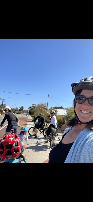The image depicts a group of people riding bicycles, with the majority wearing helmets and casual clothing, set against a backdrop of a road or path.