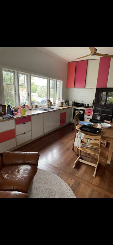 The image depicts a kitchen with a sink, stove, and cabinets, featuring a table and chairs, and a window, with a white wall and a doorway in the background.