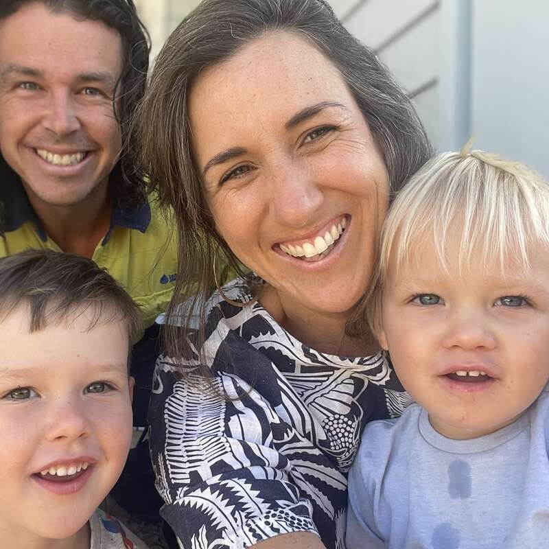 The image shows a family of four posing for a selfie, with two children and two adults, all smiling and looking at the camera.
