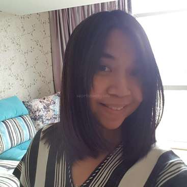 Das Bild zeigt eine Frau mit dunklen Haaren und einem gestreiften Hemd, die vor einem Bett mit blauen und weißen Kissen vor einer mit Blumen tapezierten Wand steht.