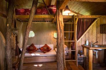 La imagen muestra una acogedora habitación con suelo de madera y una mesa, con una estantería al fondo. La habitación está bien iluminada, con un ambiente cálido y acogedor.