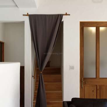 This image shows a cozy interior with wooden stairs partly covered by a dark curtain, next to a wooden door with frosted glass panels and white walls.