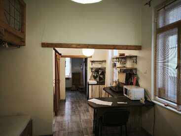 This cozy room features a small kitchenette, a desk with a microwave, bamboo blinds on windows, wooden accents, tiled floor, and shelves adorned with kitchen items.
