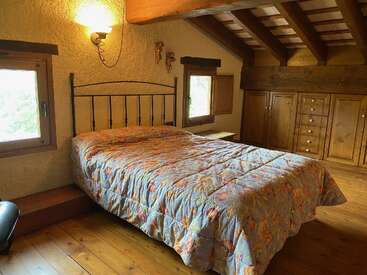 Dieses gemütliche Schlafzimmer besticht durch eine geblümte Tagesdecke, eine holzgetäfelte Decke, rustikale Holzmöbel, zwei Fenster, eine warme Beleuchtung, strukturierte Wände und eine einladende, behagliche Atmosphäre.