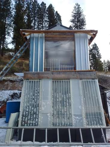 A imagem mostra um pequeno prédio de dois andares com uma escada encostada nele, situado em uma paisagem de neve com árvores ao fundo.