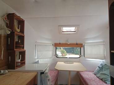 Cette image montre l'intérieur confortable d'un petit camping-car avec des étagères intégrées, des bancs rembourrés, une table, des fenêtres avec des stores et un puits de lumière au plafond.