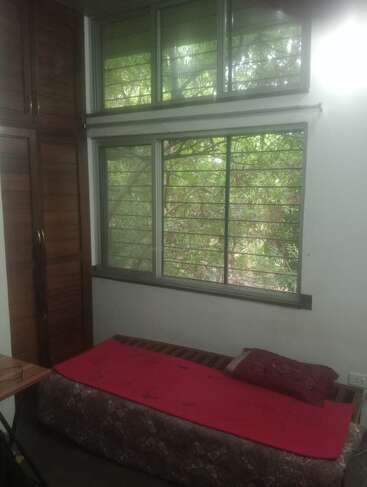 The image depicts a serene room with a bed, a window, and a closet, featuring a red blanket and a wooden cabinet, surrounded by lush greenery outside.