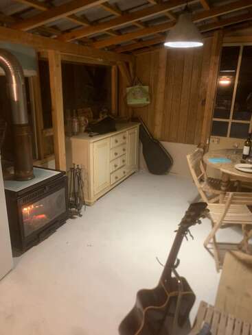 La imagen representa una acogedora habitación con una estufa de leña, una guitarra y una mesa, que destila un ambiente cálido y acogedor, posiblemente una cabaña o casa de campo.