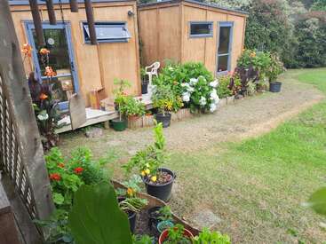 Wooden garden cabins surrounded by lush green grass, potted plants, and colorful flowers create a cozy, peaceful outdoor space with vibrant natural beauty and charm.