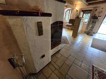 Cette pièce confortable est dotée d'un poêle en faïence rustique, de murs texturés, d'un sol en carreaux de faïence, d'un mobilier élégant, de fenêtres lumineuses, d'objets décoratifs et d'un éclairage d'ambiance chaleureux, créant ainsi une atmosphère conviviale.