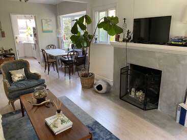 L'image représente un salon confortable avec une cheminée, un téléviseur et une salle à manger, offrant une atmosphère chaleureuse et accueillante avec des sièges confortables et des éléments décoratifs.