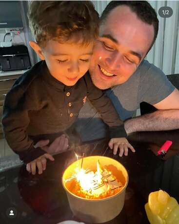 A smiling man and young boy celebrate a birthday together, leaning over a cake with lit sparklers, creating a joyful and heartwarming moment at home.