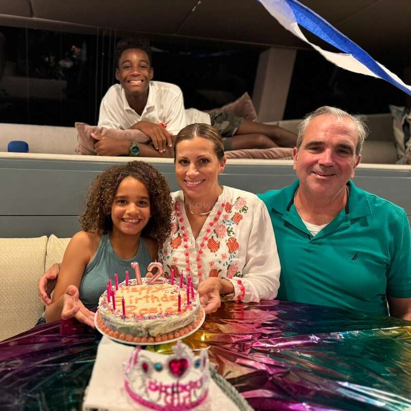 L'image montre une famille de quatre personnes célébrant un anniversaire, avec un gâteau et des bougies sur une table, et un homme et une femme assis sur un canapé derrière eux.