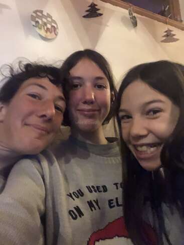 Three people are smiling closely together, appearing happy and relaxed. They are indoors, possibly at home, creating a warm and friendly atmosphere perfect for a selfie.