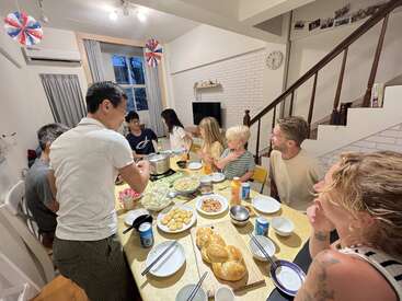 A group of people, including children and adults, gather around a dining table sharing a meal in a cozy, brightly lit home with festive decorations.