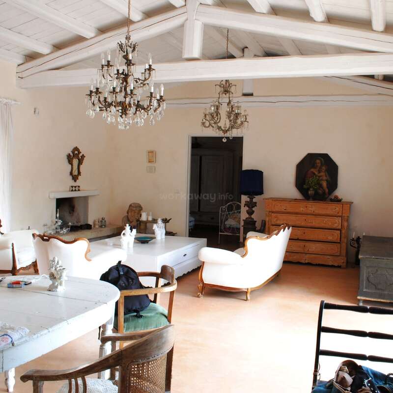 This spacious, elegant living room features white wooden beams, vintage chandeliers, classic sofas, an ornate fireplace, wooden furniture, soft lighting, and tasteful decorative accents for charm.