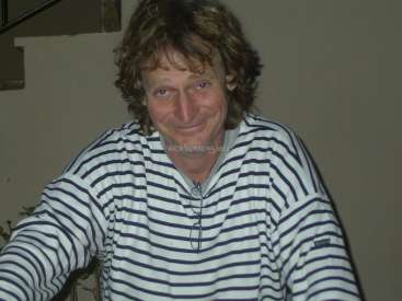 L'image représente un homme aux cheveux bruns bouclés de longueur moyenne, vêtu d'une chemise à rayures blanches et bleues, avec un filigrane au centre.