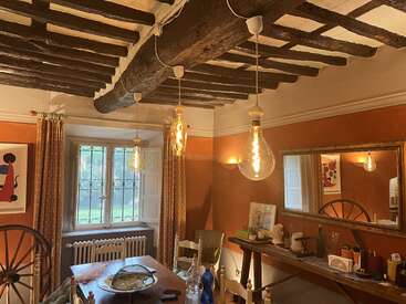 Dieser gemütliche, rustikale Essbereich besticht durch freiliegende Holzbalken, hängende Edison-Glühbirnen, orangefarbene Wände, einen großen Spiegel, eine eklektische Einrichtung und ein Fenster mit gemusterten Vorhängen. Gemütliche Atmosphäre.