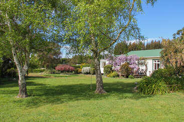 Ein charmantes Haus mit grünem Dach steht inmitten üppiger Gärten und blühender Bäume. Das helle Sonnenlicht bringt den leuchtend grünen Rasen und die schönen Frühlingsblumen zum Leuchten.