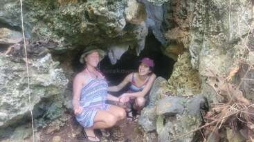 Zwei Frauen stehen am Eingang einer Felshöhle. Die eine meditiert mit geschlossenen Augen, während die andere lächelt. Beide genießen gemeinsam ein Abenteuer in der Natur.
