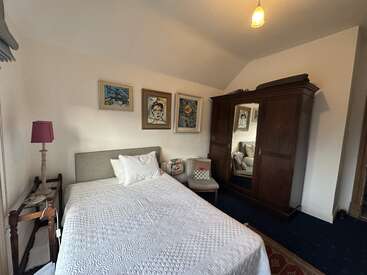 Esta acogedora habitación cuenta con una cama individual con ropa de cama blanca, tres cuadros enmarcados encima, un armario de madera con espejo, una mesita auxiliar, una lámpara y una silla acolchada.