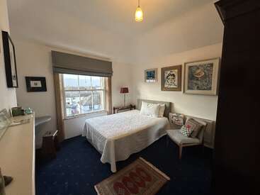 Une chambre confortable et bien éclairée avec un lit double, une literie blanche, des œuvres d'art accrochées au mur, une table d'appoint avec une lampe et une fenêtre donnant sur la ville.