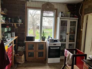Une cuisine rustique et chaleureuse, avec des murs et des meubles en bois, une fenêtre donnant sur un jardin, une cuisinière, des placards blancs, un micro-ondes et divers ustensiles de cuisine soigneusement rangés.