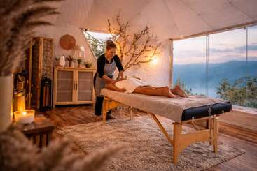 Une salle de spa paisible offrant une vue sur les montagnes, un éclairage chaleureux et une décoration inspirée de la nature. Un thérapeute procède à un massage relaxant sur une table, créant ainsi une atmosphère sereine.