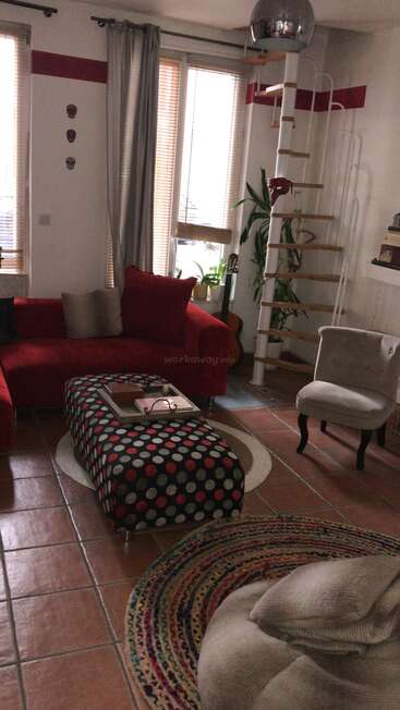 A imagem mostra uma sala de estar aconchegante com um sofá vermelho, uma escada em espiral e um tapete vibrante, exalando uma atmosfera calorosa e convidativa.