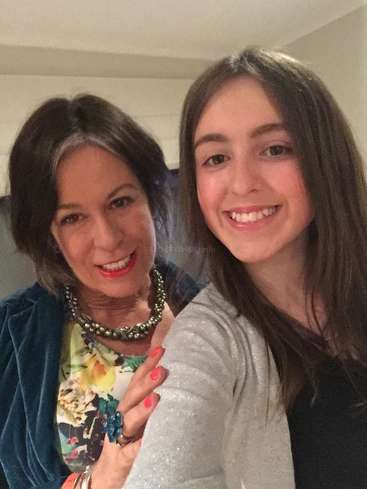 Das Bild zeigt zwei Frauen, die für ein Selfie posieren. Die eine trägt ein geblümtes Oberteil und die andere eine graue Strickjacke, beide lächeln in die Kamera.